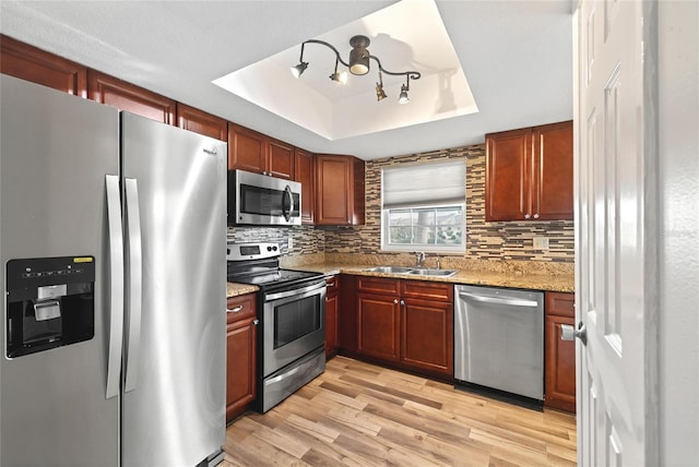 kitchen featuring light hardwood / wood-style floors, sink, a tray ceiling, light stone countertops, and stainless steel appliances