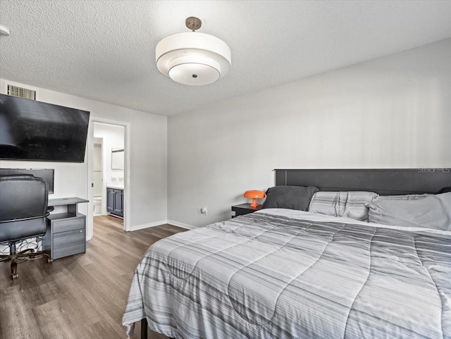 bedroom with a textured ceiling, dark hardwood / wood-style flooring, and ensuite bath