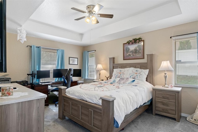 bedroom with ceiling fan, a raised ceiling, and light colored carpet