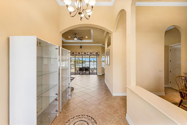 hallway featuring light tile patterned floors, a raised ceiling, ornamental molding, and a notable chandelier