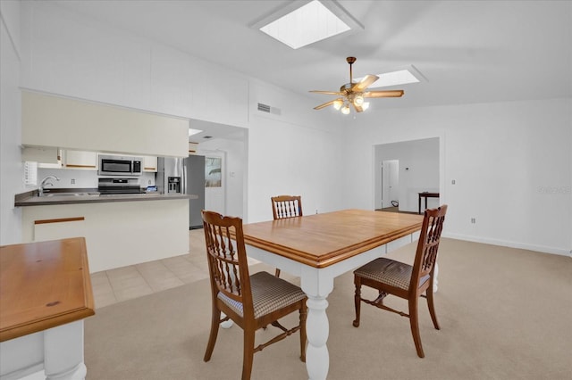 carpeted dining area featuring ceiling fan, lofted ceiling with skylight, and sink