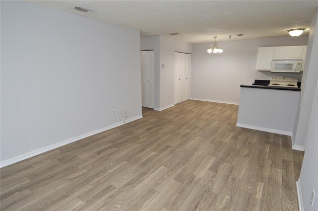 unfurnished living room with light hardwood / wood-style floors, a textured ceiling, and a chandelier