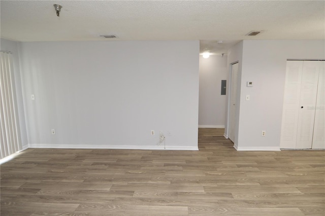 unfurnished room with electric panel, light hardwood / wood-style floors, and a textured ceiling