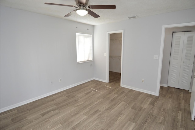 unfurnished bedroom featuring a textured ceiling, a spacious closet, light hardwood / wood-style flooring, and ceiling fan