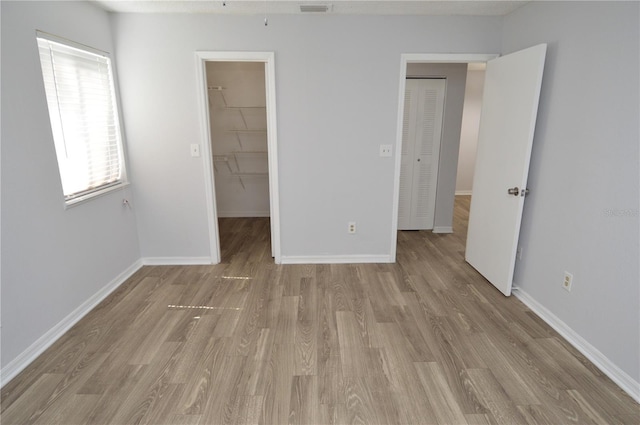 unfurnished bedroom featuring a walk in closet, a closet, and light wood-type flooring