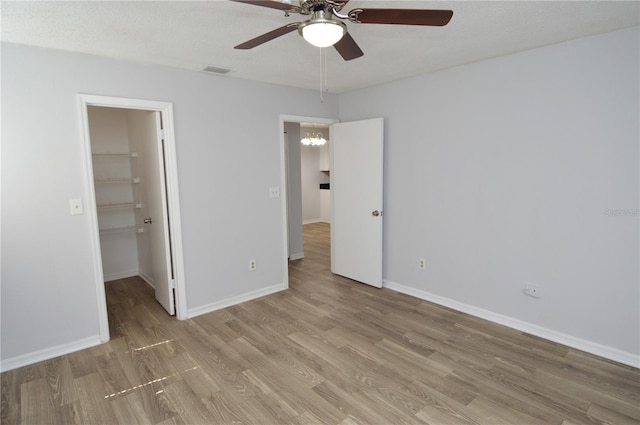 unfurnished bedroom with a walk in closet, ceiling fan, light wood-type flooring, a textured ceiling, and a closet