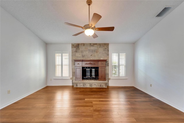 unfurnished living room with wood-type flooring, a textured ceiling, a tile fireplace, and a wealth of natural light