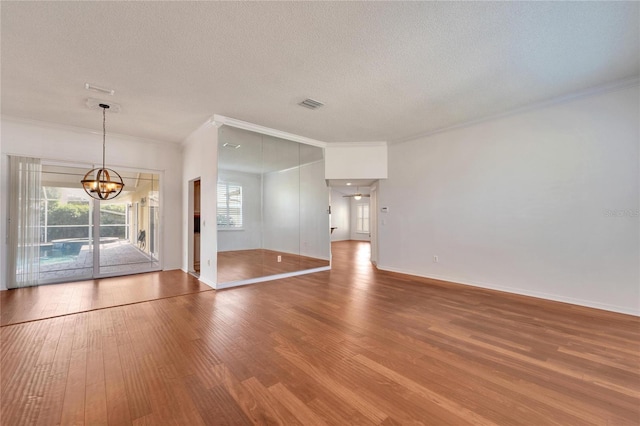 unfurnished room with a textured ceiling, wood-type flooring, ornamental molding, and a chandelier