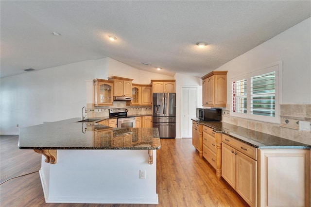 kitchen with a breakfast bar area, vaulted ceiling, light wood-type flooring, kitchen peninsula, and stainless steel appliances