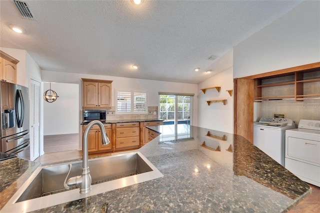 kitchen featuring lofted ceiling, sink, washer and dryer, dark stone countertops, and stainless steel appliances