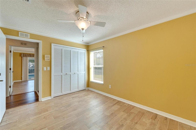 unfurnished bedroom with crown molding, light hardwood / wood-style flooring, a closet, and a textured ceiling