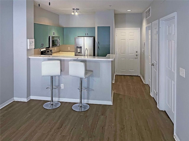 kitchen featuring green cabinets, dark hardwood / wood-style flooring, kitchen peninsula, a breakfast bar area, and appliances with stainless steel finishes