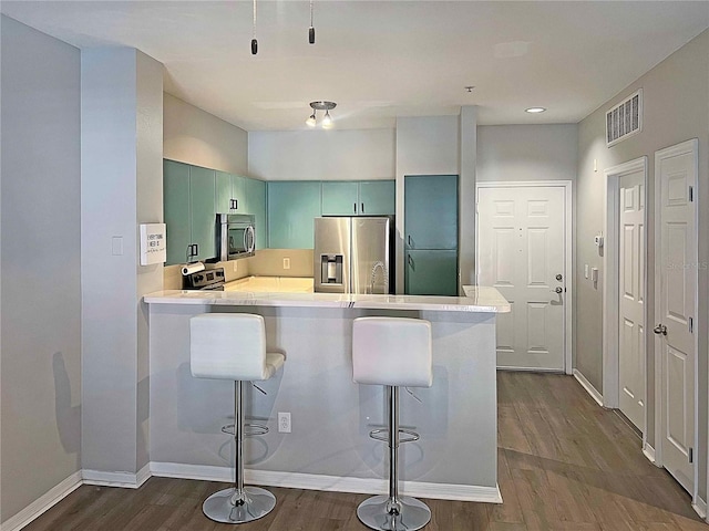 kitchen featuring stainless steel appliances, a kitchen breakfast bar, green cabinets, dark hardwood / wood-style floors, and kitchen peninsula