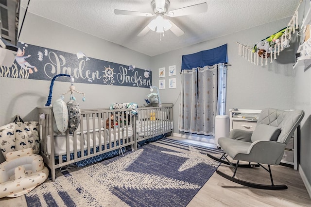 bedroom featuring ceiling fan, wood-type flooring, a textured ceiling, and a nursery area