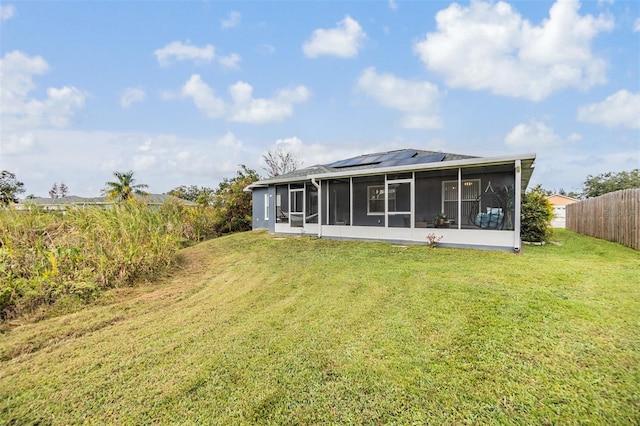 rear view of property featuring a sunroom, solar panels, and a yard