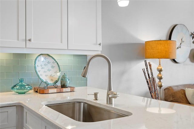 interior details with white cabinets, backsplash, light stone countertops, and sink