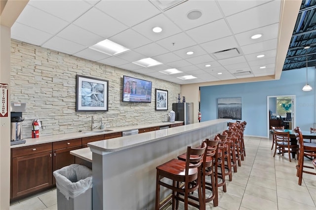 kitchen with a kitchen breakfast bar, a paneled ceiling, sink, a center island, and light tile patterned flooring