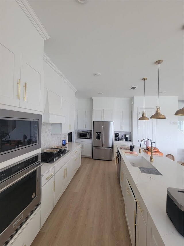 kitchen with premium range hood, appliances with stainless steel finishes, pendant lighting, white cabinets, and light wood-type flooring