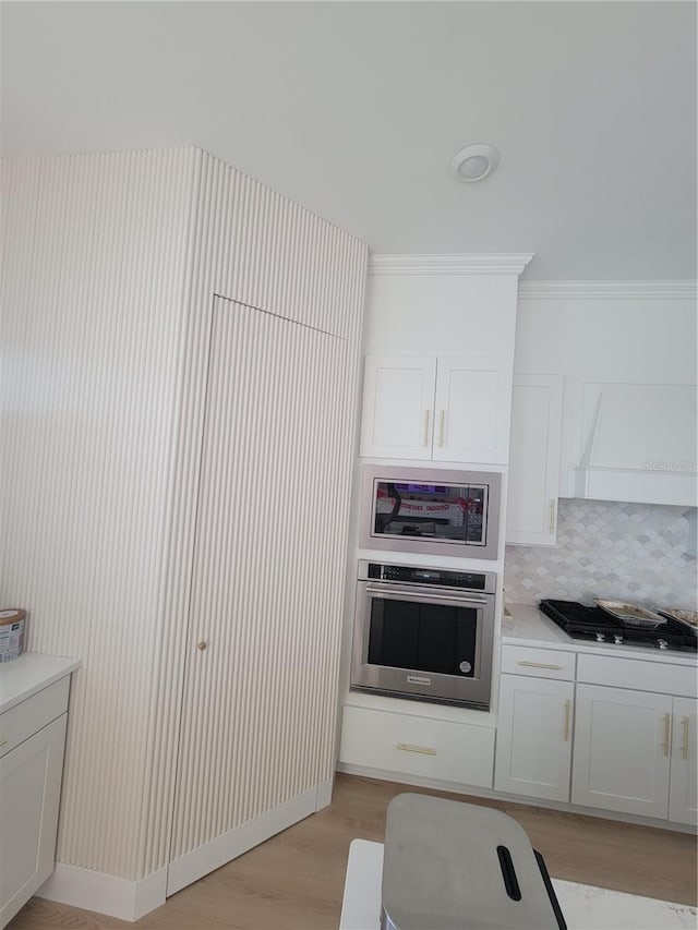 kitchen featuring appliances with stainless steel finishes, light wood-type flooring, backsplash, ornamental molding, and white cabinetry