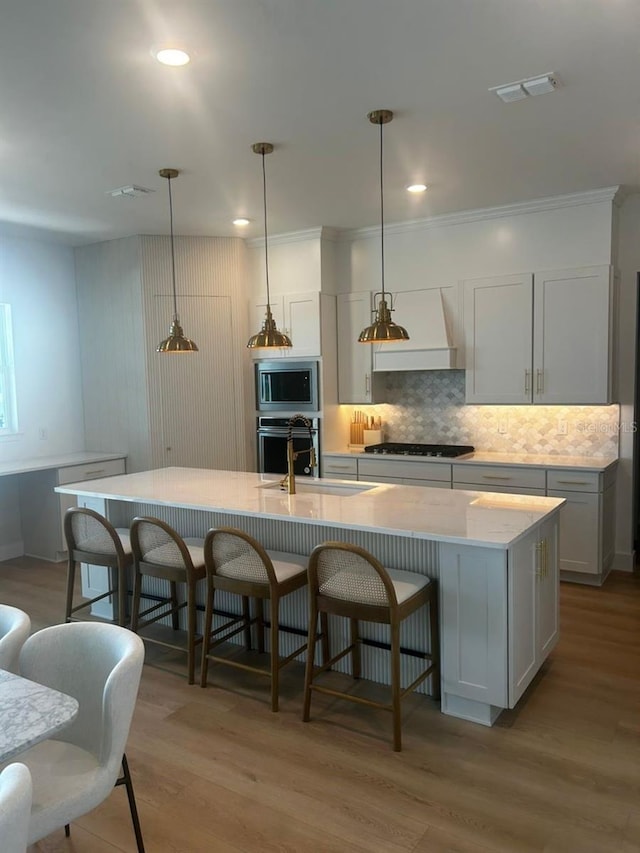 kitchen featuring a large island with sink, stainless steel appliances, premium range hood, and light hardwood / wood-style floors