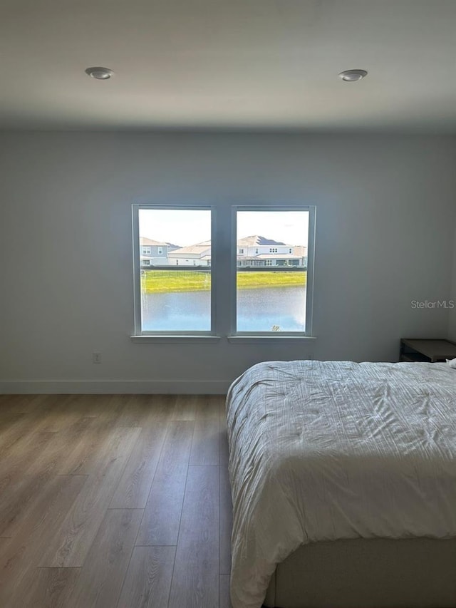 bedroom featuring multiple windows, a water view, and light hardwood / wood-style floors