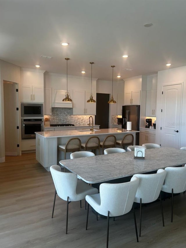 kitchen with stainless steel appliances, backsplash, a sink, an island with sink, and a kitchen breakfast bar