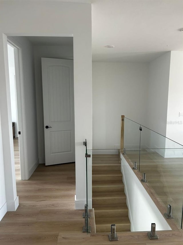 hallway featuring light wood finished floors, baseboards, and an upstairs landing