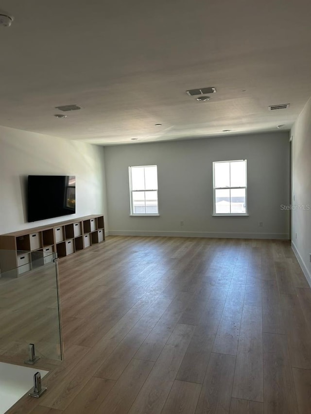 unfurnished living room featuring visible vents, baseboards, and wood finished floors