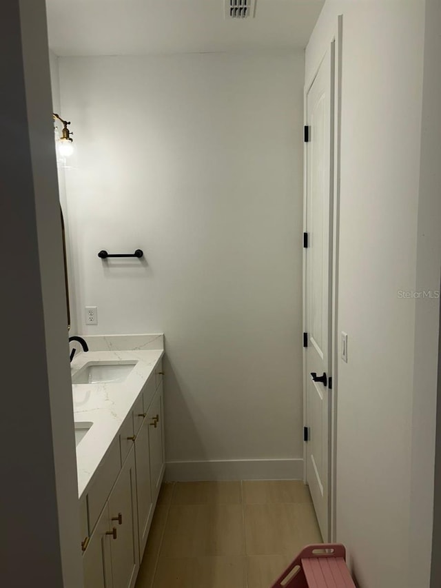 bathroom featuring a sink, visible vents, baseboards, tile patterned floors, and double vanity