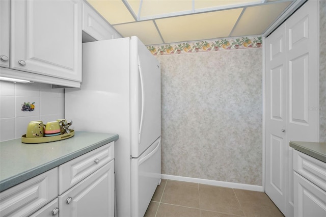 kitchen with light tile patterned floors, light countertops, backsplash, freestanding refrigerator, and white cabinets