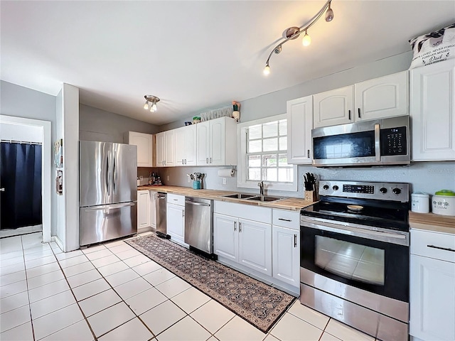 kitchen with appliances with stainless steel finishes, light tile patterned floors, white cabinetry, and sink