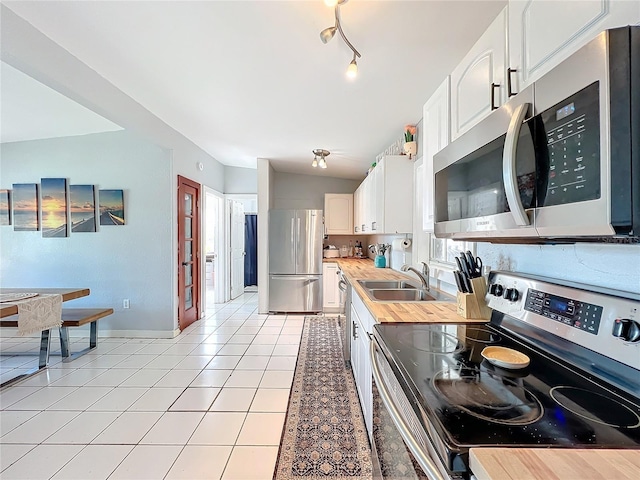 kitchen with stainless steel appliances, vaulted ceiling, sink, light tile patterned floors, and white cabinetry