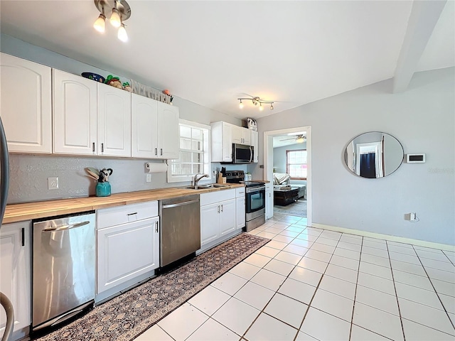 kitchen featuring sink, stainless steel appliances, light tile patterned floors, wooden counters, and white cabinets