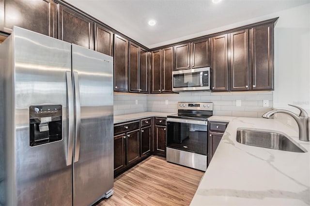 kitchen featuring backsplash, light stone counters, stainless steel appliances, sink, and light hardwood / wood-style floors