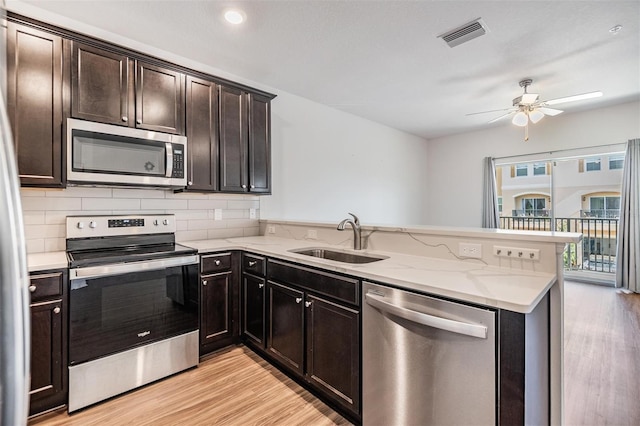 kitchen with sink, light wood-type flooring, light stone counters, kitchen peninsula, and stainless steel appliances