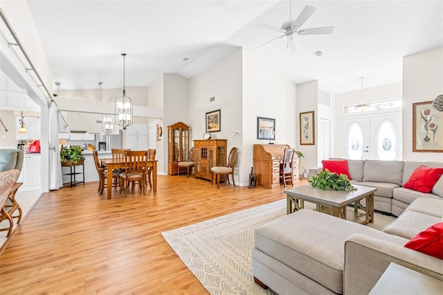 living room with ceiling fan, high vaulted ceiling, wood-type flooring, and a textured ceiling