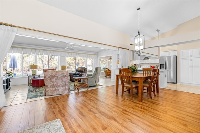 dining area with ceiling fan with notable chandelier, lofted ceiling, and light wood-type flooring