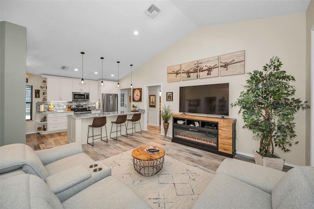1012 Osprey Ct, Tarpon Springs, FL 34689 - living room featuring light wood-type flooring, lofted ceiling, recessed lighting, and a glass covered fireplace