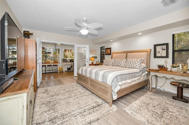 bedroom featuring multiple windows, ceiling fan, a textured ceiling, and light wood-type flooring