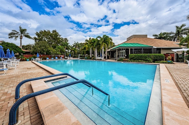 view of pool featuring a sunroom, a patio, and a hot tub