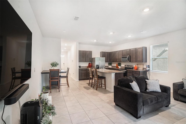 kitchen featuring dark brown cabinetry, stainless steel appliances, a kitchen breakfast bar, a kitchen island with sink, and light tile patterned floors