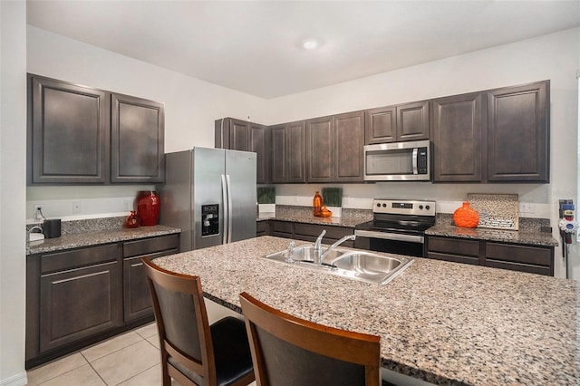 kitchen featuring a kitchen bar, dark brown cabinetry, stainless steel appliances, sink, and light tile patterned floors