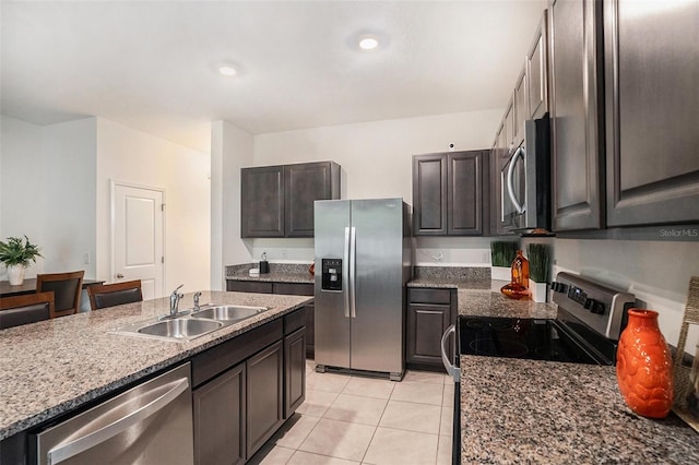 kitchen with light stone countertops, dark brown cabinets, stainless steel appliances, sink, and light tile patterned floors