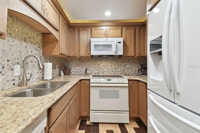 kitchen with light stone countertops, light wood-type flooring, backsplash, white appliances, and sink