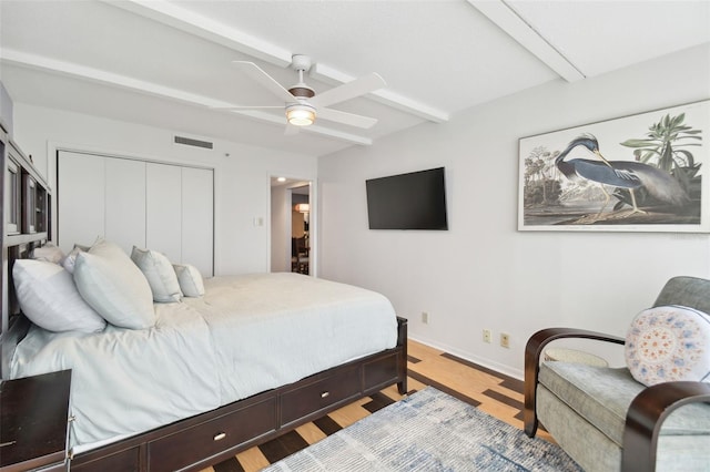 bedroom with beamed ceiling, hardwood / wood-style floors, a closet, and ceiling fan