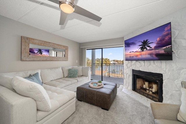 carpeted living room with a stone fireplace, ceiling fan, and a textured ceiling