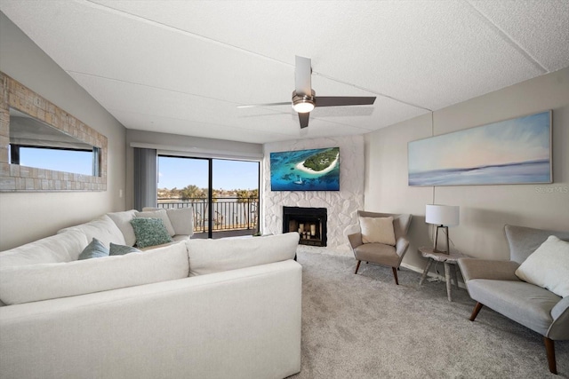 carpeted living room featuring a stone fireplace, ceiling fan, and a textured ceiling