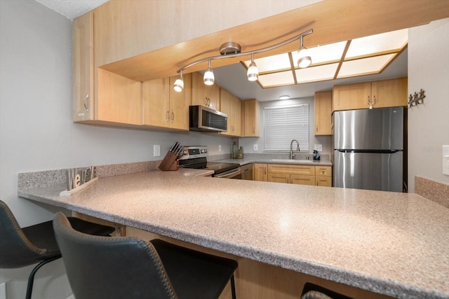 kitchen with kitchen peninsula, light brown cabinetry, a kitchen breakfast bar, stainless steel appliances, and sink