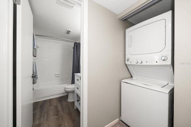 washroom with a textured ceiling, dark hardwood / wood-style floors, and stacked washer / dryer