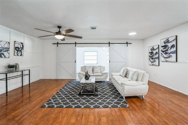 living room featuring a barn door, ceiling fan, hardwood / wood-style floors, and a textured ceiling